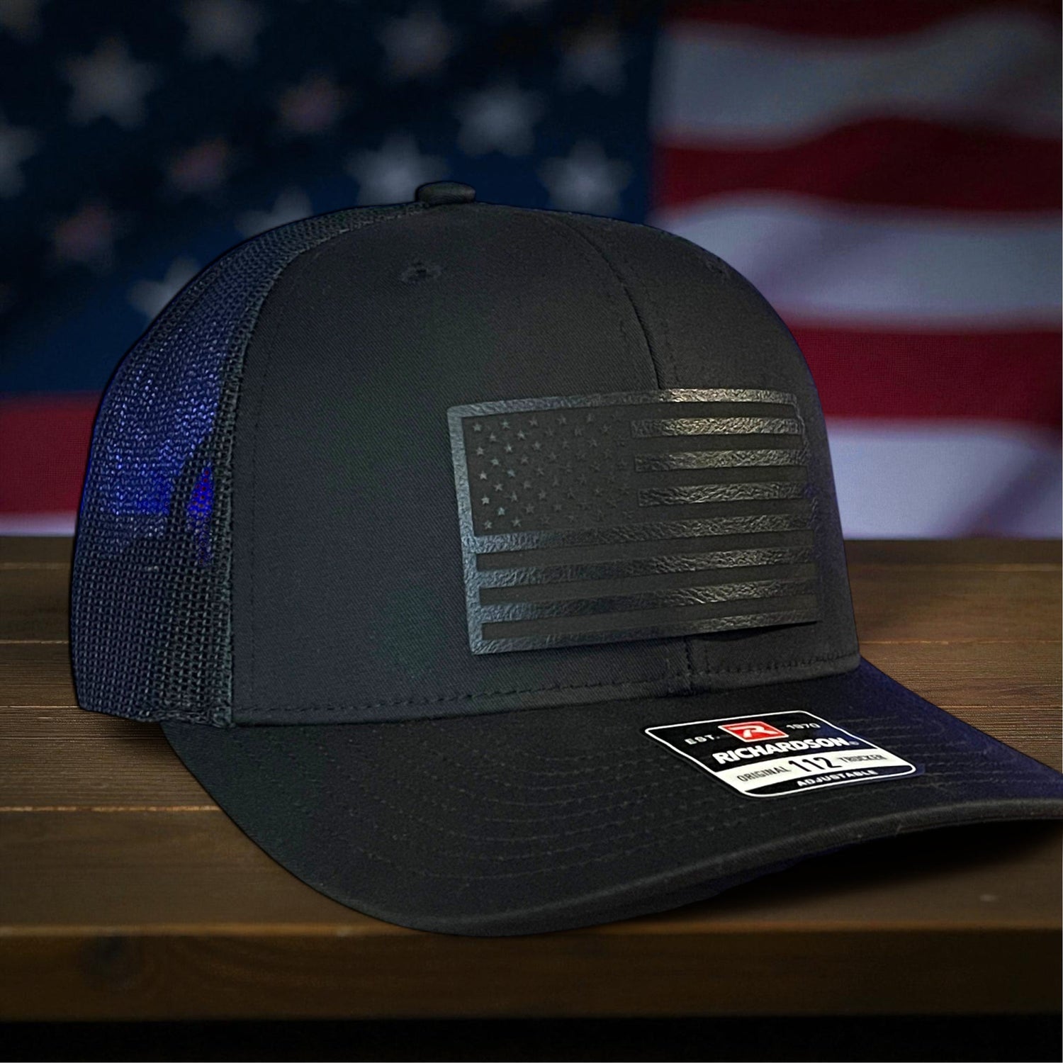 Blue trucker hat with eagle emblem and '250 Years of America' design on a wooden surface with an American flag in the background.